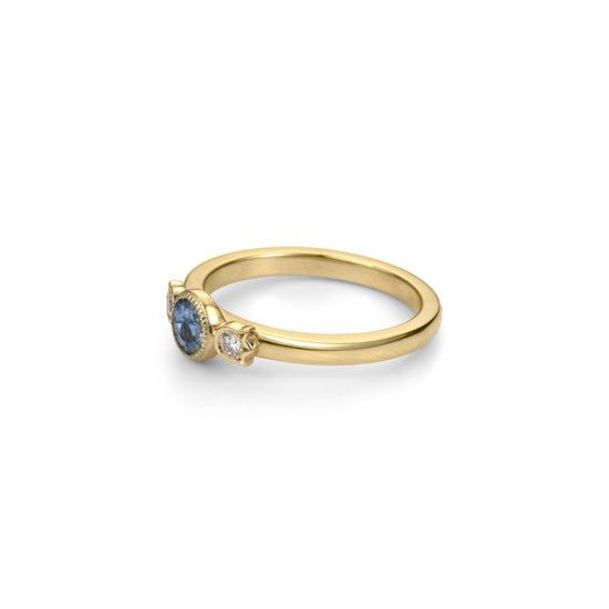 Load image into Gallery viewer, Yellow gold stackable ring with round beaded bezel set Montana blue sapphire and diamonds in flower setting on each side in profile view.
