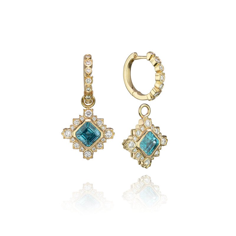 Yellow gold hinged huggie earrings with diamonds set in alternating round and flower shaped bezels with removeable charms containing centre bezel set octagonal shape blue zircons and fancy set diamonds surrounding.