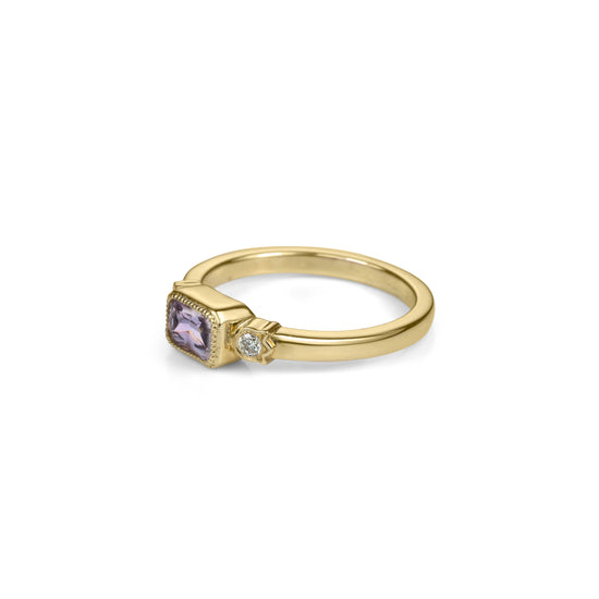 Yellow gold ring with horizontally set radiant cut lilac purple sapphire in millegrained bezel and diamonds in flower shaped setting on each side in profile view