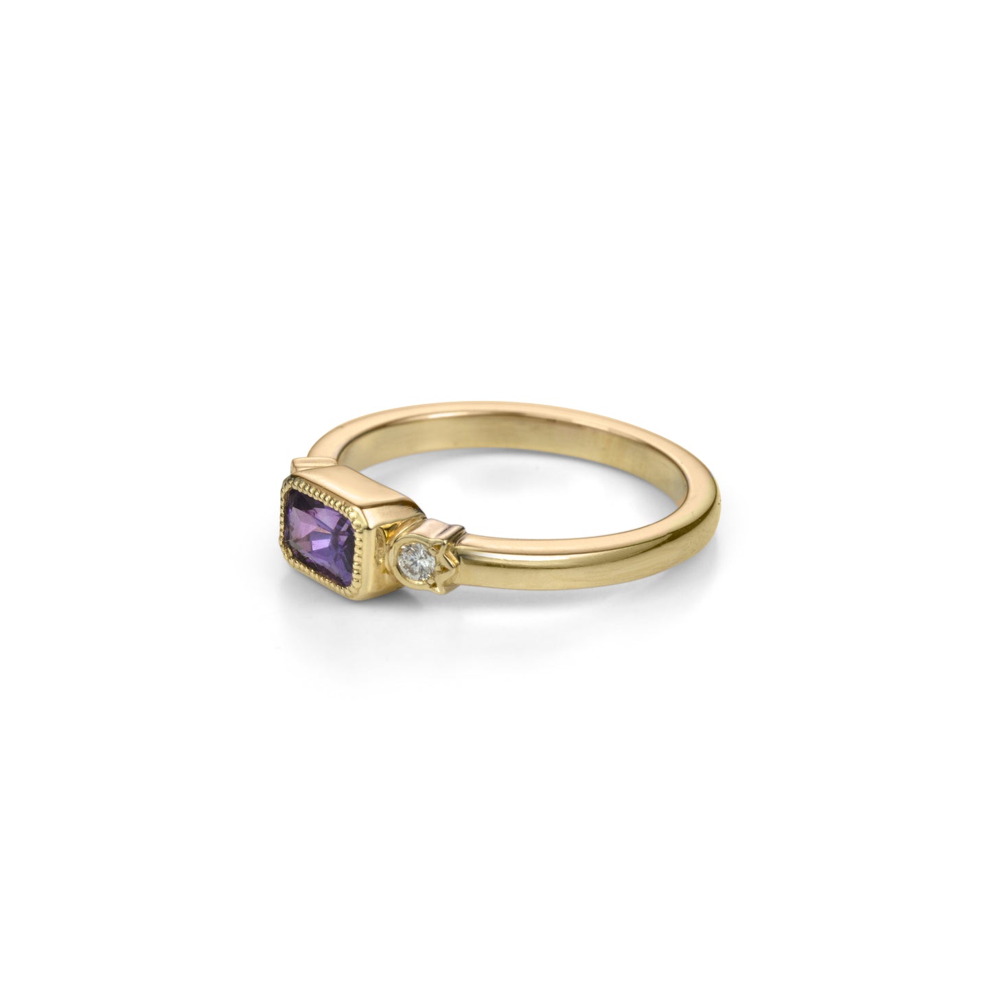 Yellow gold ring with horizontally set radiant cut royal purple sapphire in millegrained bezel and diamonds in flower shaped setting on each side in profile view.